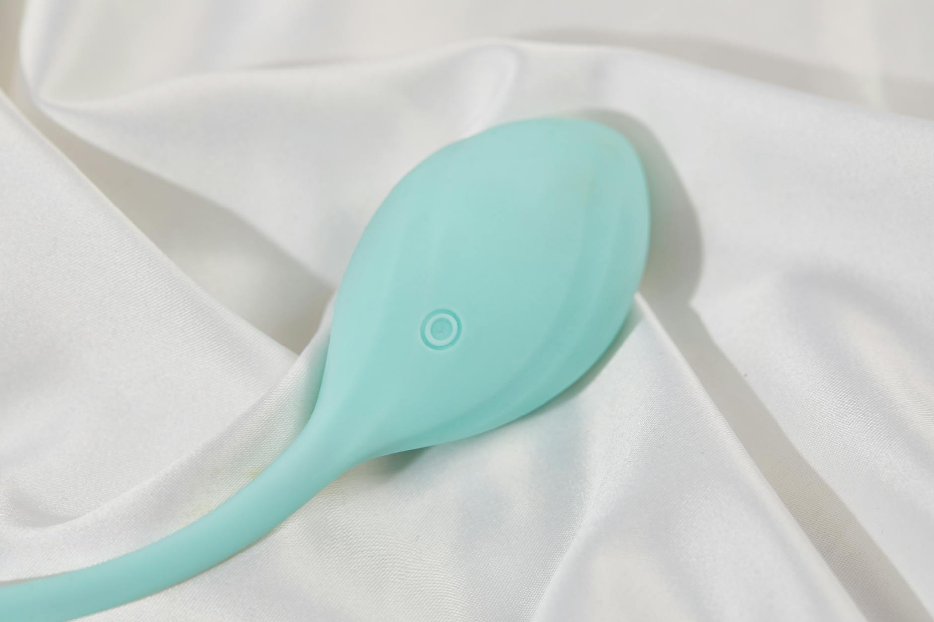 A teal lemon clitoral vibrator on white silk fabric