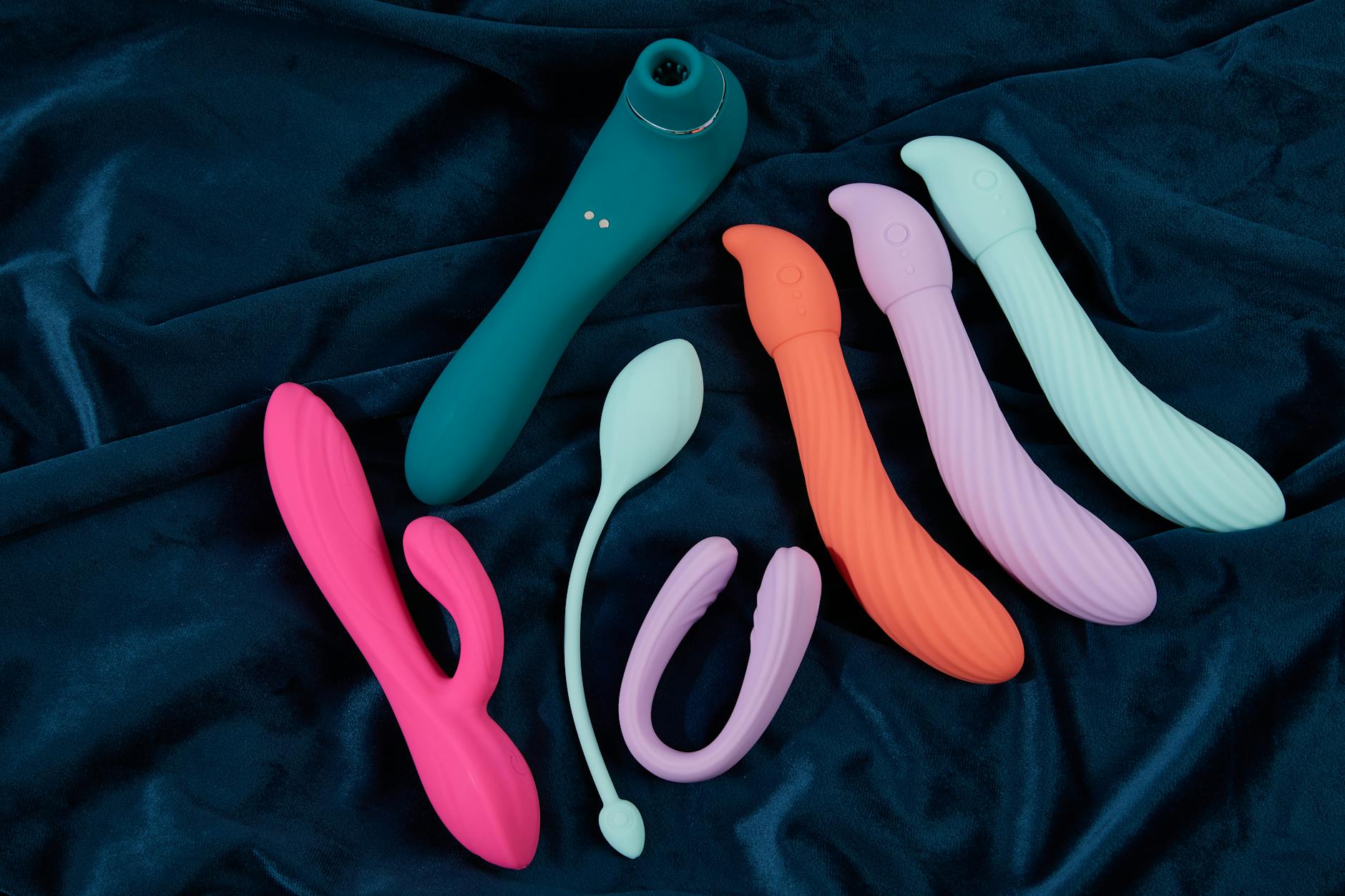 Colección vibrante de juguetes sexuales de silicona en tonos variados sobre tela azul oscura