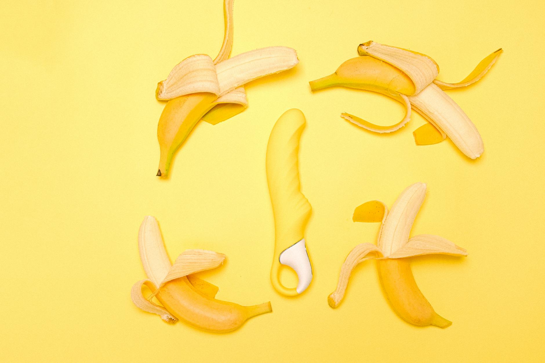 A bright yellow silicone lemon vibrator surrounded by fresh lemons on a yellow background