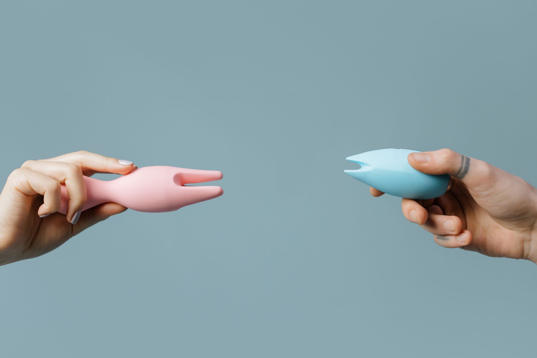 Two hands holding soft silicone vibrators in muted tones against a calming pastel background.