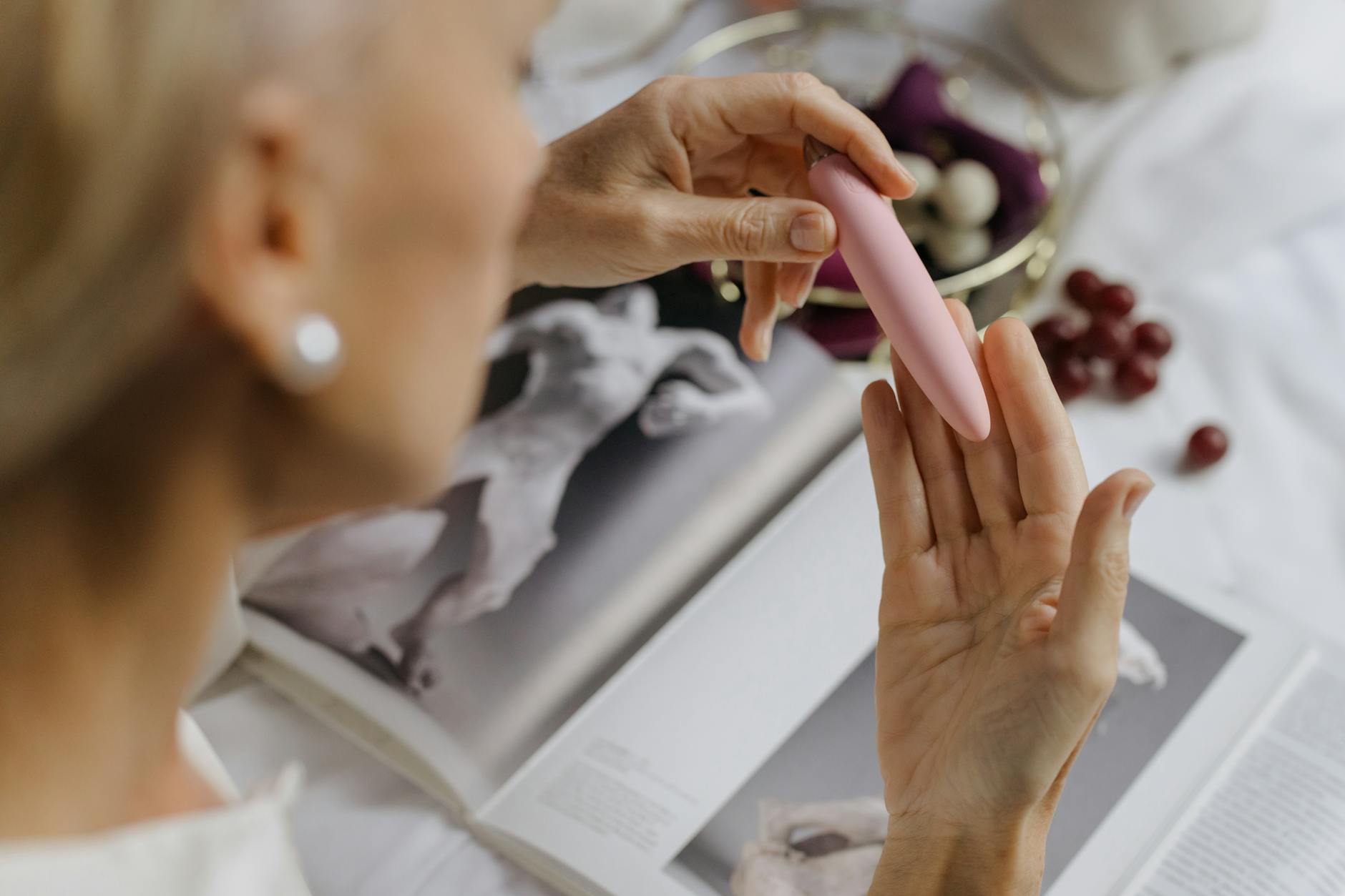 Close-up of a hand gently holding a pink vibrator next to art books, symbolizing the return to personal pleasure and self-discovery.