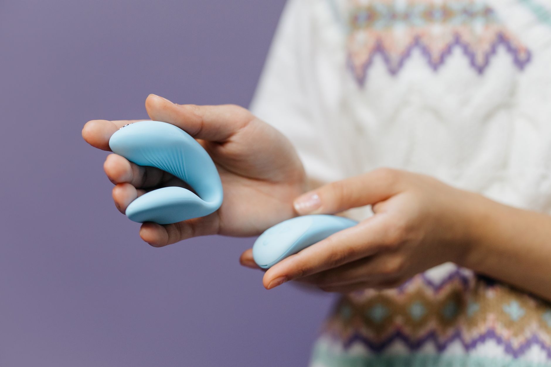 Dos manos sostienen un vibrador rosa y azul suave contra un fondo pastel.