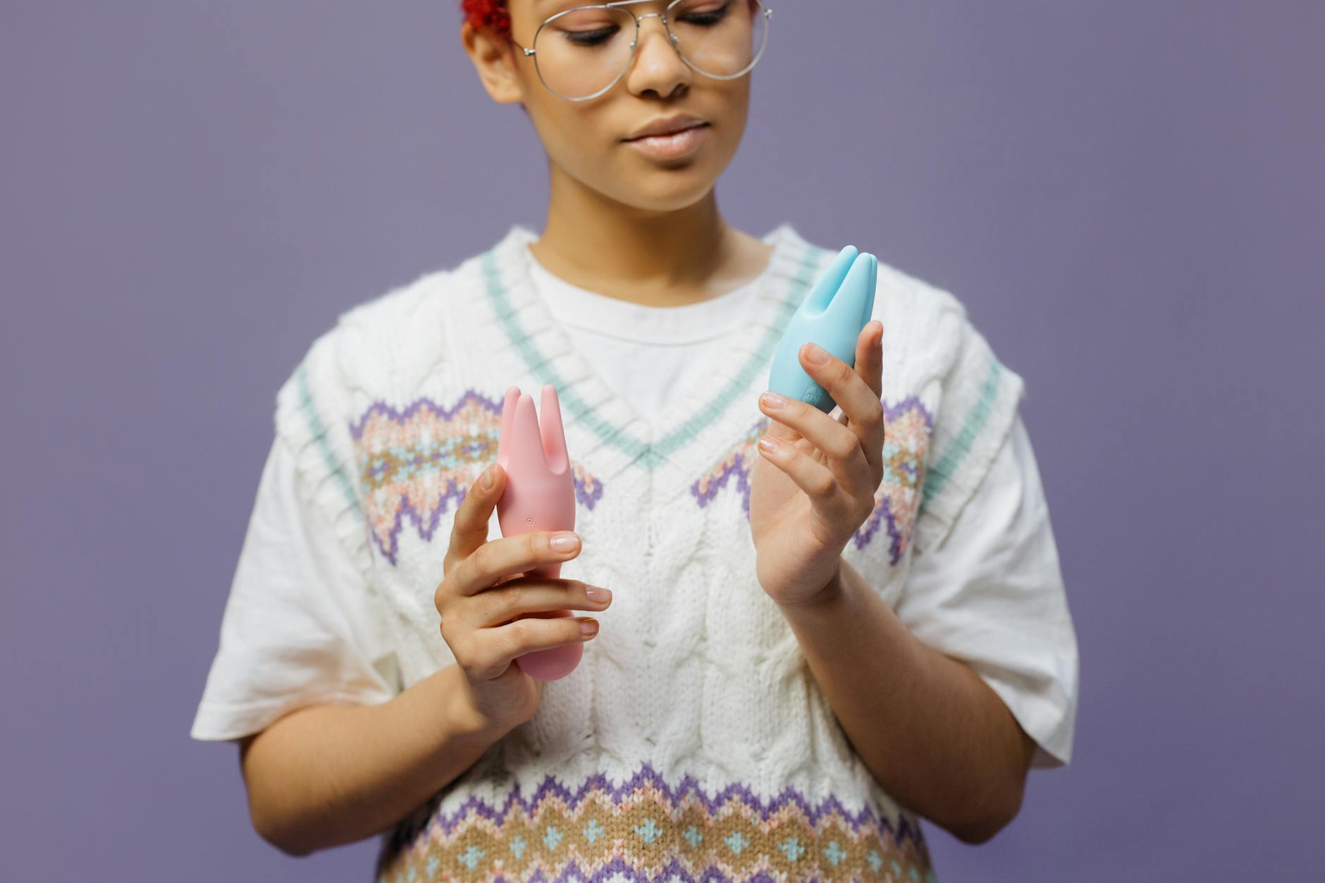 Woman holding blue and pink silicone vibrators, contemplative expression